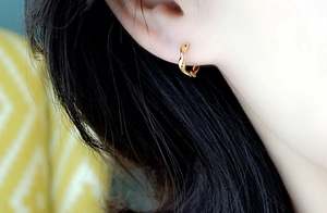Detailed view of gold twisted wave hoop earring worn on ear with polished finish