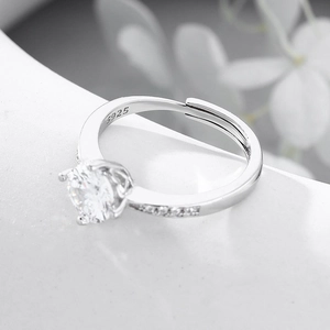 Anello a corona in argento S925 con zircone da 6,5 mm su sfondo bianco con fiori sfocati