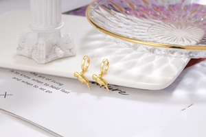 Detailed close-up of 18K gold parrot drop earrings on a vintage white display stand