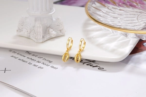 Close-up of golden hoop earrings featuring shell pendants on a white marble background