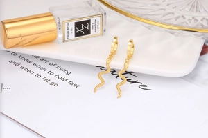 Macro view of golden snake earrings with embossed scale textures on a white tray
