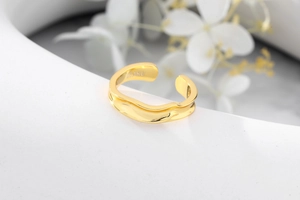 Close-up of wavy gold Mobius ring with IOAKU engraving on white floral background