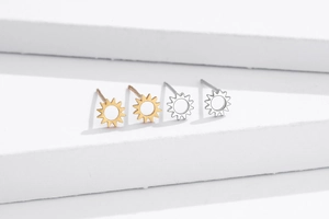 Close-up of small hollow sun stud earrings in silver and gold on a white stone base
