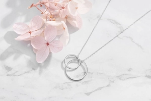 Detail of interlocking silver double ring necklace on white marble background