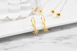 Detailed close-up of gold S925 sterling silver hoop earrings with sunburst star charms