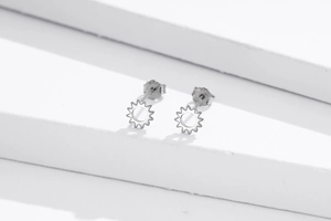Macro detail of sun-shaped silver earrings showing the S925 hallmark on a white stair background