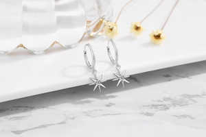 Detail of silver S925 star drop earrings with sparkling zircon on a marble surface