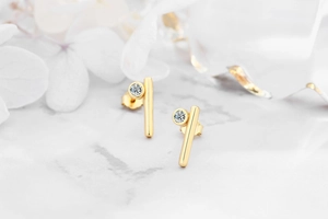 Close-up of golden vertical bar earrings with a round zircon stone on marble background
