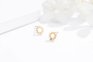 Macro shot of minimalist gold sunflower stud earrings on a clean white display pedestal