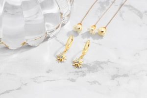 Macro shot of gold star dangle earrings with zircon on white marble surface