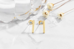 Detail of gold geometric earrings with zircon inlay on a marble background scene