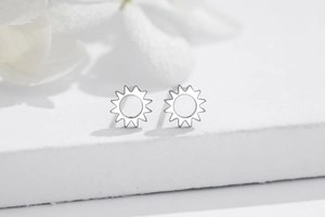 Macro shot of minimalist silver sun-shaped stud earrings on a white marble surface