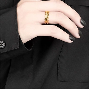 Close-up of golden leaf olive branch ring worn by a model against a dark background