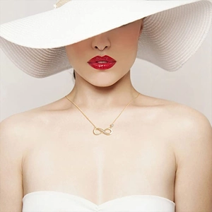 Detail of elegant gold infinity pendant necklace with small crystals on female model