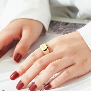 Détail d'une bague chevalière carrée géométrique dorée portée à la main avec vernis rouge