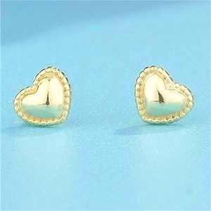 Détail de boucles d'oreilles cœur dorées avec bord perlé sur un fond bleu clair épuré