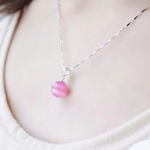Gros plan d'un pendentif en pierre œil de chat rose sur une chaîne argentée torsadée
