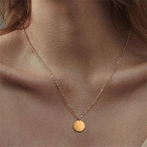 Close-up of a minimalist golden round disc pendant necklace worn on the collarbone