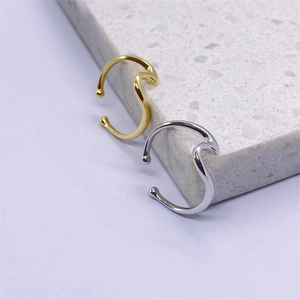 Ear cuff minimalisti con design a onde in oro e argento su superficie di marmo