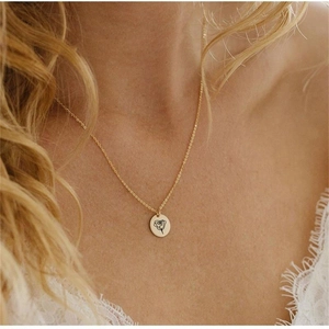 Close-up of gold disc pendant necklace featuring a minimalist engraved rose pattern