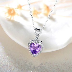 Vue macro du pendentif cœur avec pierre violette et détail de nœud sur plat blanc