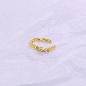 Detail of a minimalist gold-plated C-shaped ear cuff set with three clear zircons