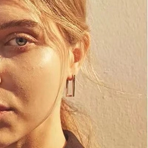 Close-up of minimalist rectangular sterling silver hoop earrings in gold finish on model