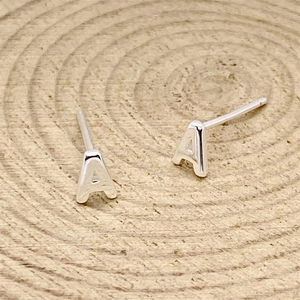Close-up of silver letter A stud earrings on a natural wood grain circular base