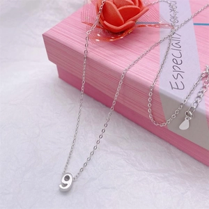 Macro detail of silver number 9 pendant with cross chain on pink gift box background