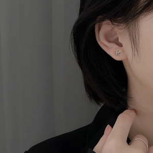 Close-up of minimalist S925 sterling silver letter K stud earring worn by a model