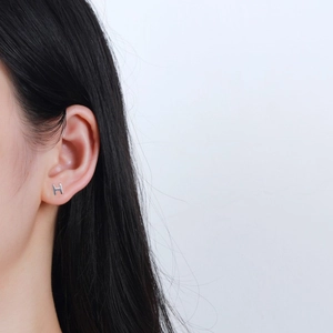 Detail view of a minimalist S925 sterling silver letter H stud earring worn on the ear