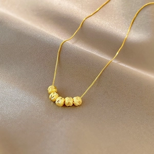 Détail de cinq perles dorées texturées sur une chaîne maille miroir sur de la soie
