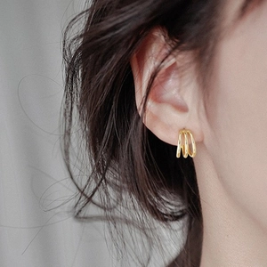 Détail de créoles dorées minimalistes à trois rangs portées par un mannequin chic