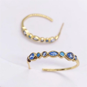 Close-up of gold-plated C-shaped earrings with inlaid blue geometric gemstones