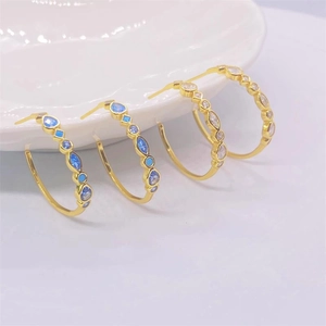Élégantes créoles dorées avec zircons turquoise et saphir posées sur céramique