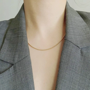 Gros plan d'un collier ras du cou à billes dorées porté avec un blazer gris élégant