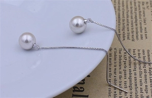 Detail of 8mm white pearl earring with S925 silver long box chain on vintage background
