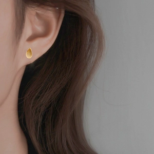 Detail of teardrop stud earring with brushed gold finish and minimalist metal texture