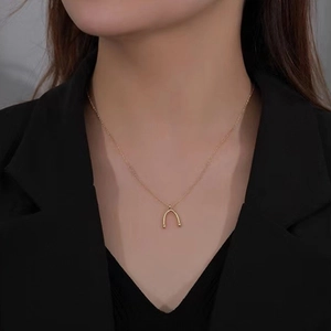 Close-up of a gold minimalist wishbone pendant necklace on a model wearing black
