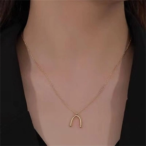 Detail of a minimalist gold-plated wishbone pendant necklace worn by a female model
