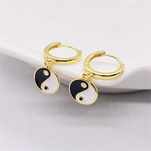 Close-up of gold S925 silver Tai Chi Yin Yang drop earrings on a white ceramic tray