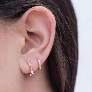 Close-up of gold geometric spiked hoop earrings with zircon pavé on a model's ear