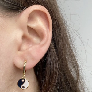 Macro shot of gold Yin Yang hoop earrings with blue and white enamel on a model