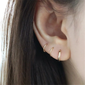 Close-up of three minimalist polished gold hoop earrings worn on ear with layered effect