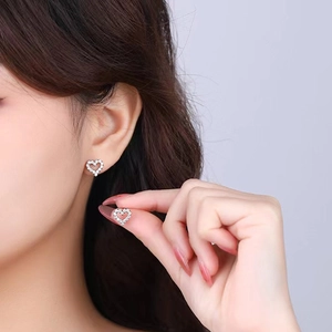 Detailed view of hollow heart silver earrings with pavé crystals on a model's ear