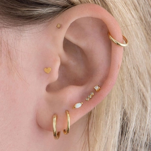 Close-up of gold heart stud earrings and hoops with opal stones on model ear