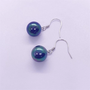Dettaglio macro di orecchini con perle iridescenti su ganci in argento sfondo viola