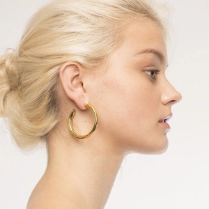 Close-up of polished gold-plated thick hoop earrings worn by a model on a neutral background