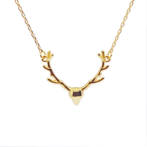 Close-up of golden deer antler pendant on a delicate cross chain necklace