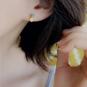 Close-up of small pineapple stud earring with yellow and green gemstones on model's ear